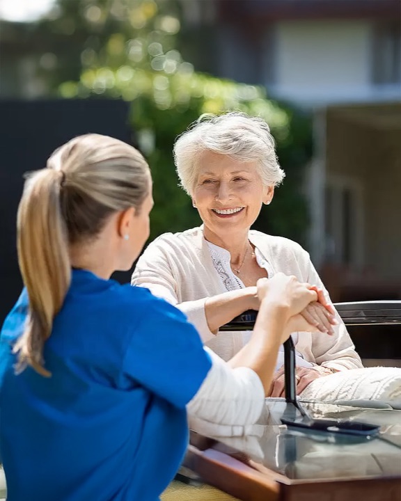 Ergotherapeutin im Gespräch mit einer lachenden Seniorin im Freien