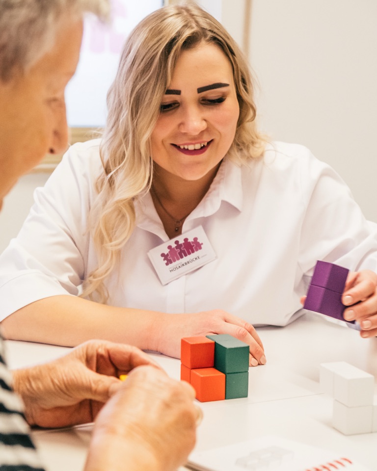 Mareike Grimm übt mit einer Patientin das Stapeln farbiger Holzwürfel