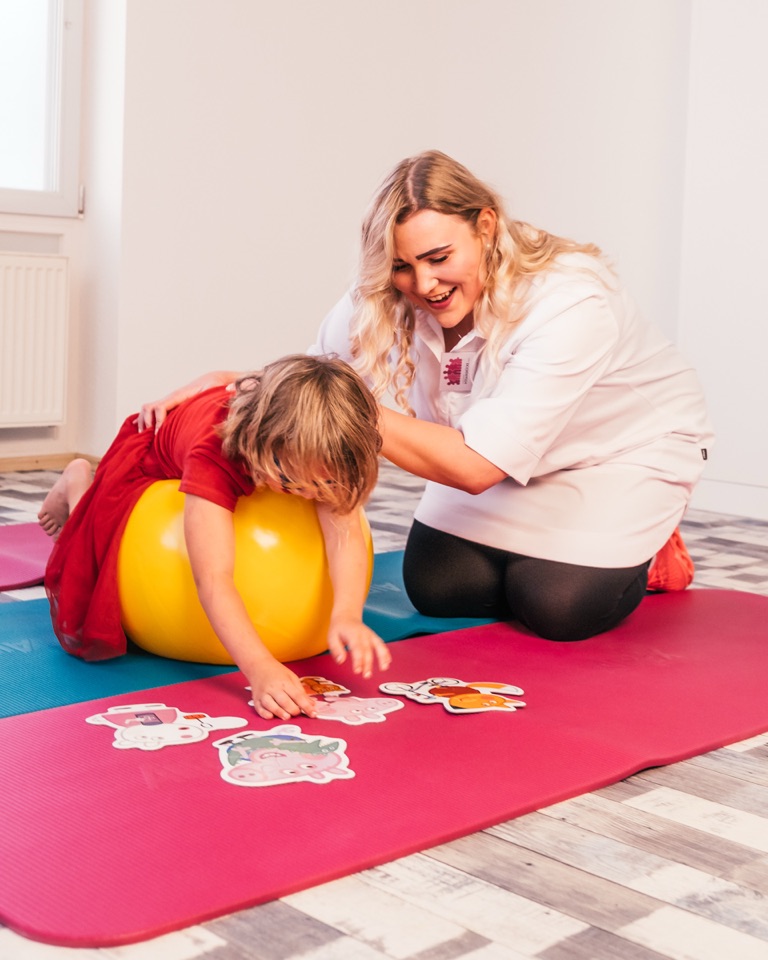 Mädchen liegt auf einem gelben Gymnastikball, Mareike Grimm stützt es